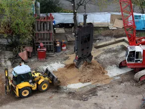A diaphragm-wall grab over the guide wall, beside a red crawler crane