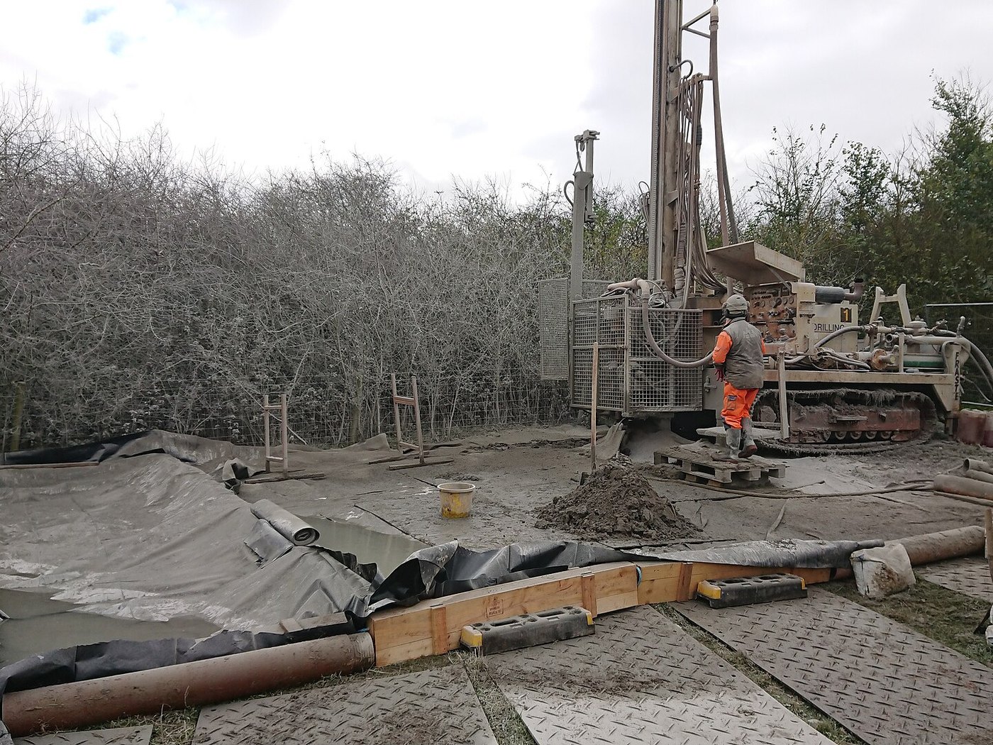 A borehole drilling rig beside its lined mud pit