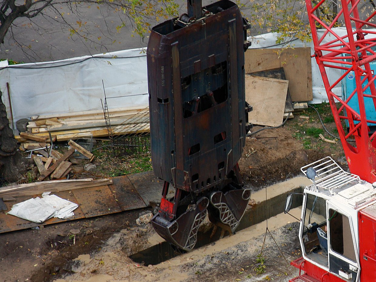 Seen from above, a grab lowering into a slurry-filled diaphragm-wall panel between guide walls