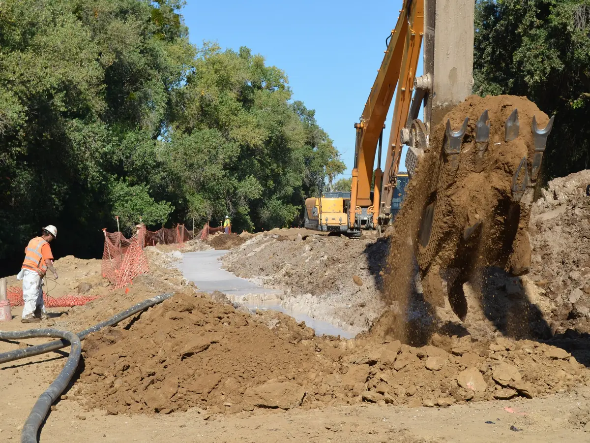 An excavator placing backfill into a slurry-supported cut-off trench