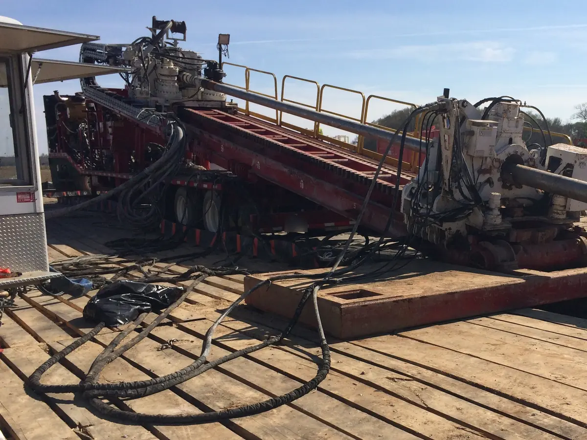 An HDD rig on timber mats, its drill string angled into the ground